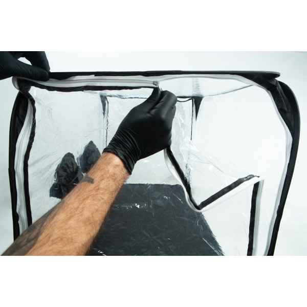 A person in black gloves unzipping a clear plastic enclosure with a black frame.