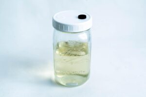A glass Kilner jar with a white lid, filled halfway with a clear liquid, as seen in guides on how to make MEA mix in the microwave, sits on a white background.
