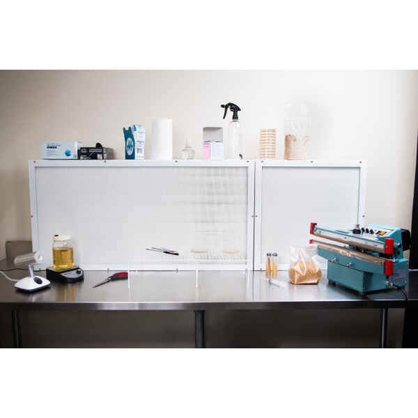 A clean lab workspace features a Laminar Flow Hood HEPA Airfilter H14 with pre-filter 60x60x35cm, equipment, petri dishes, jars, and a vacuum sealer on a stainless steel table.