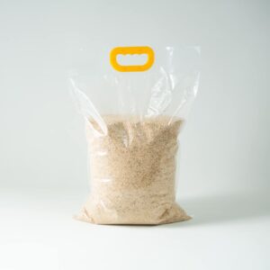 A clear plastic bag containing Certified Organic Biodynamic Rye berry grain, with a yellow handle, displayed on a white background.