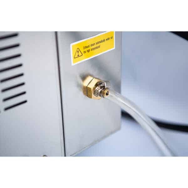 Clear tube connected to a brass fitting on a metal machine; warning label about high temperature nearby.