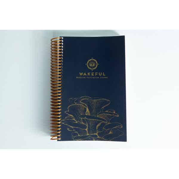 Dark blue spiral-bound Wakeful Mushroom Cultivation Journal by Australian mycologist Caine Barlow, featuring gold mushrooms on the cover.