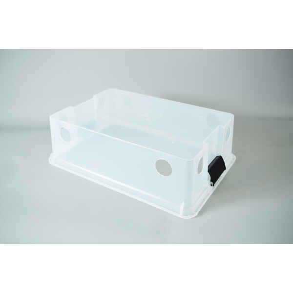 A clear plastic monotub kit with circular holes and a black catch, designed for growing mushrooms, is placed on a light grey surface.
