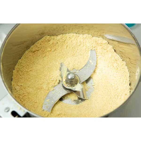 Close-up of Freeze-Dried Mushroom Lion’s Mane in a food processor, showing finely ground yellow powder and sharp metal blades inside.