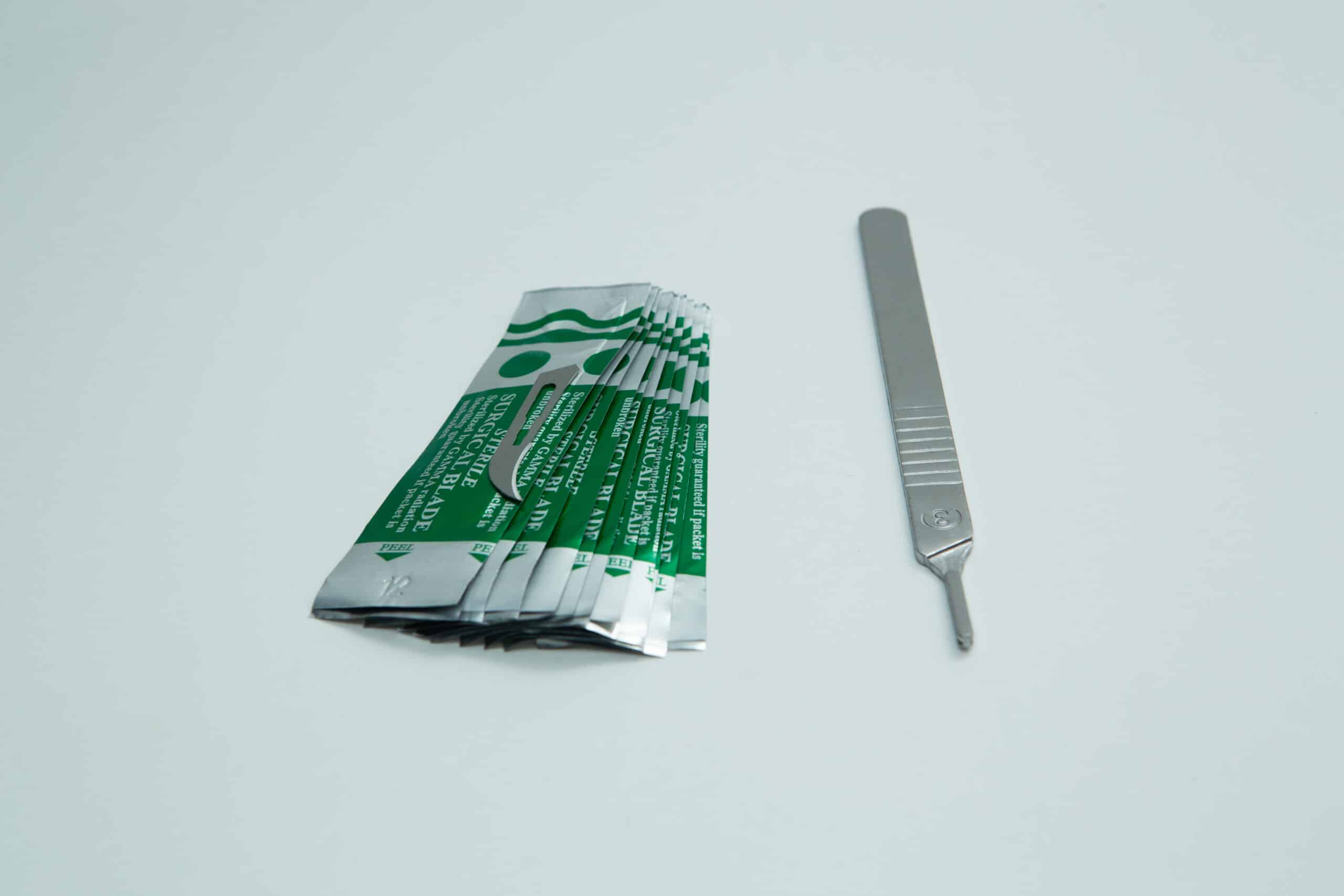 Scalpel handle #3 and blades | Mycology 6 A metal scalpel handle and several individually wrapped scalpel blades on a white background.