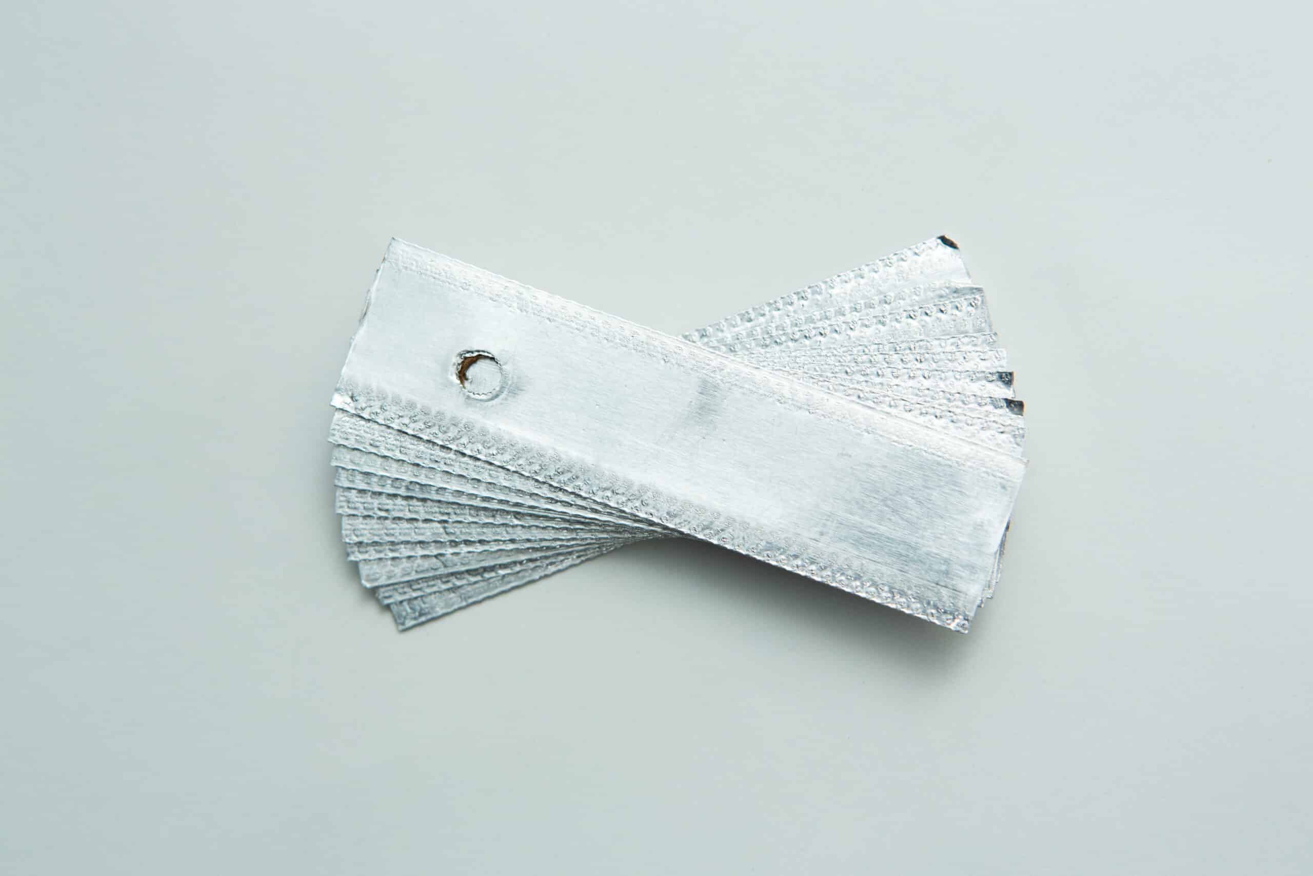 Aluminium Log Labelling Tags - Weather Safe 2 A stack of silver metal texture samples held together by a metal ring on a light grey surface.