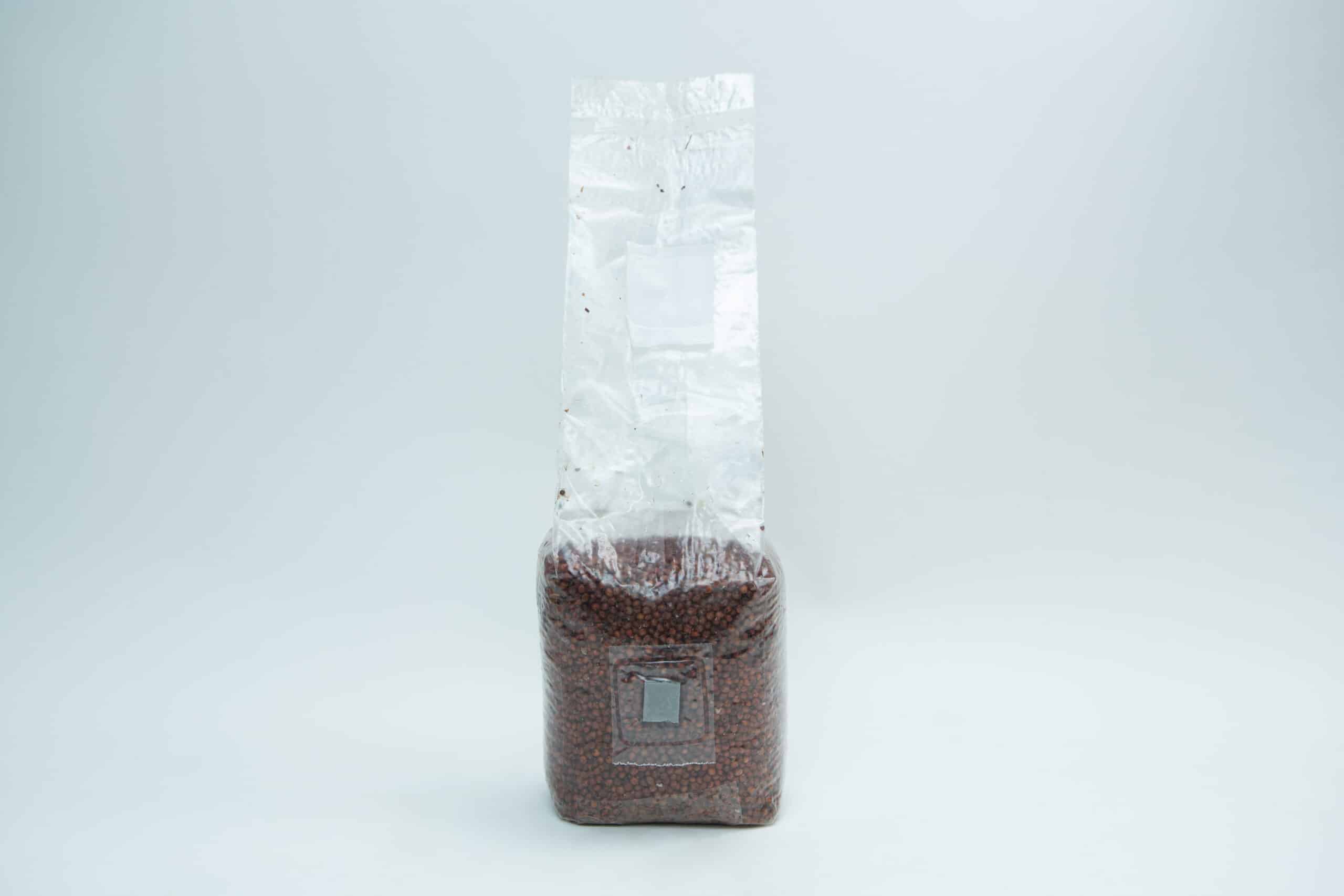Sorghum(Milo) Pre sterilised for mushroom cultivation w/inj port and air-filter 1kg 2 A sealed, clear plastic bag filled with small brown beans, standing upright against a white background.