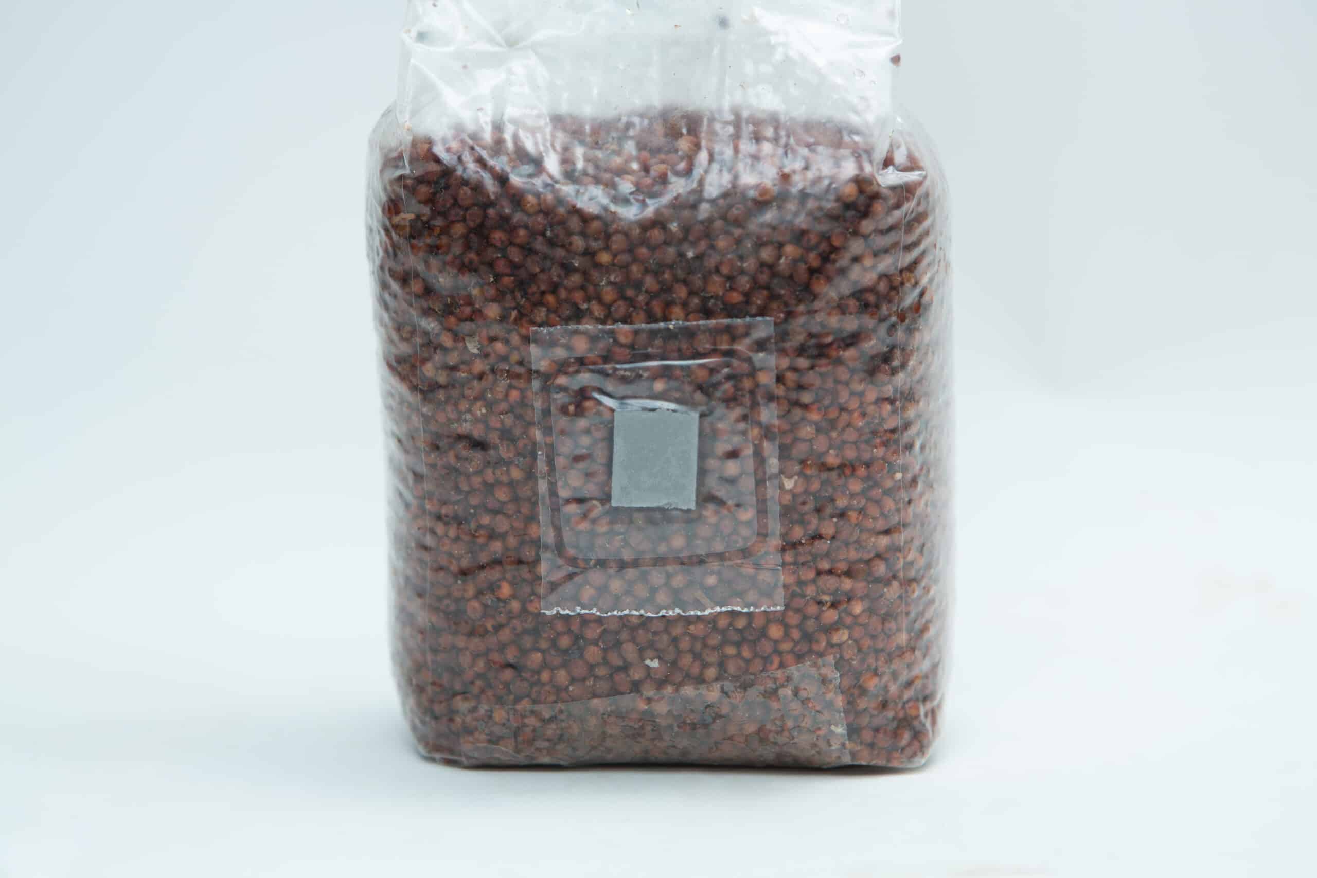 Sorghum(Milo) Pre sterilised for mushroom cultivation w/inj port and air-filter 1kg 1 A sealed plastic bag filled with small brown seeds or grains on a plain white background.